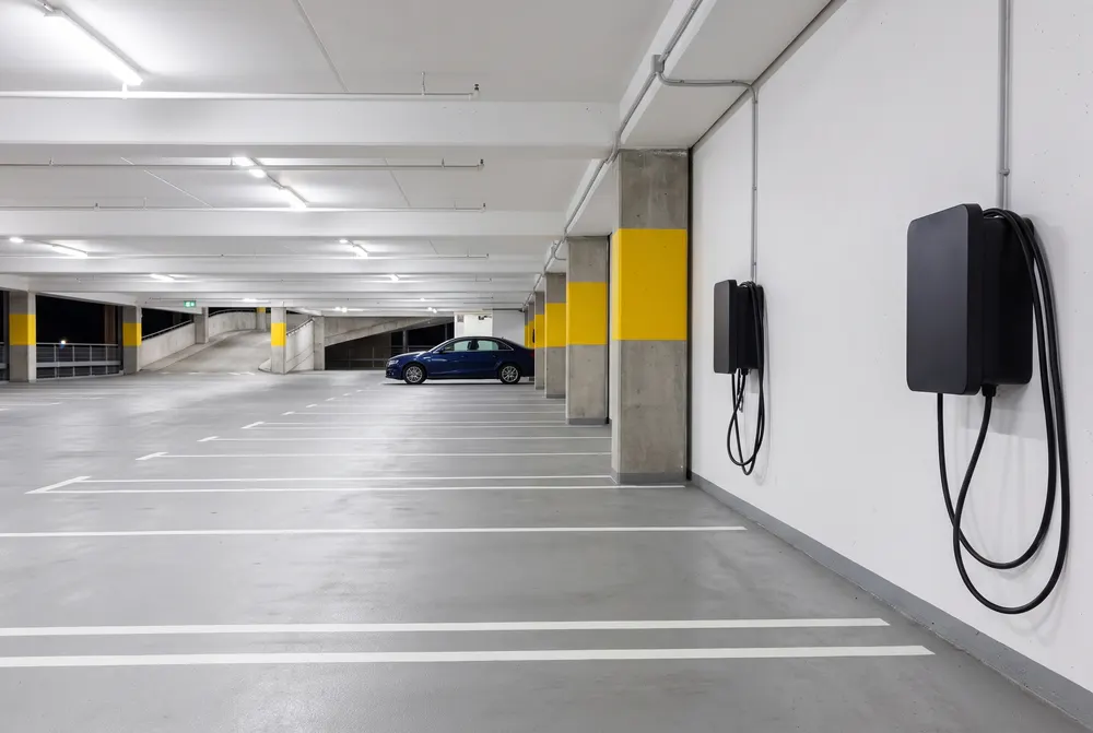 Generated scene: an empty level of a bright parking garage with two wall-mounted electric car chargers and yellow-banded pillars.